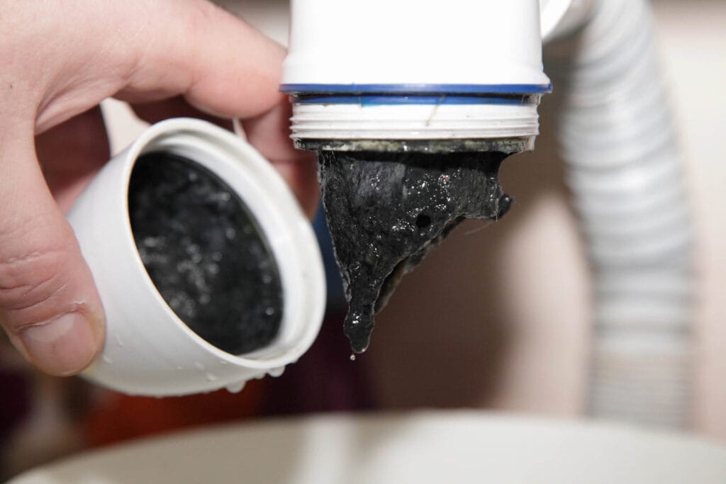 Hand holding a container pouring dark, thick sludge from a drain, illustrating drain cleaning services for stubborn clogs.