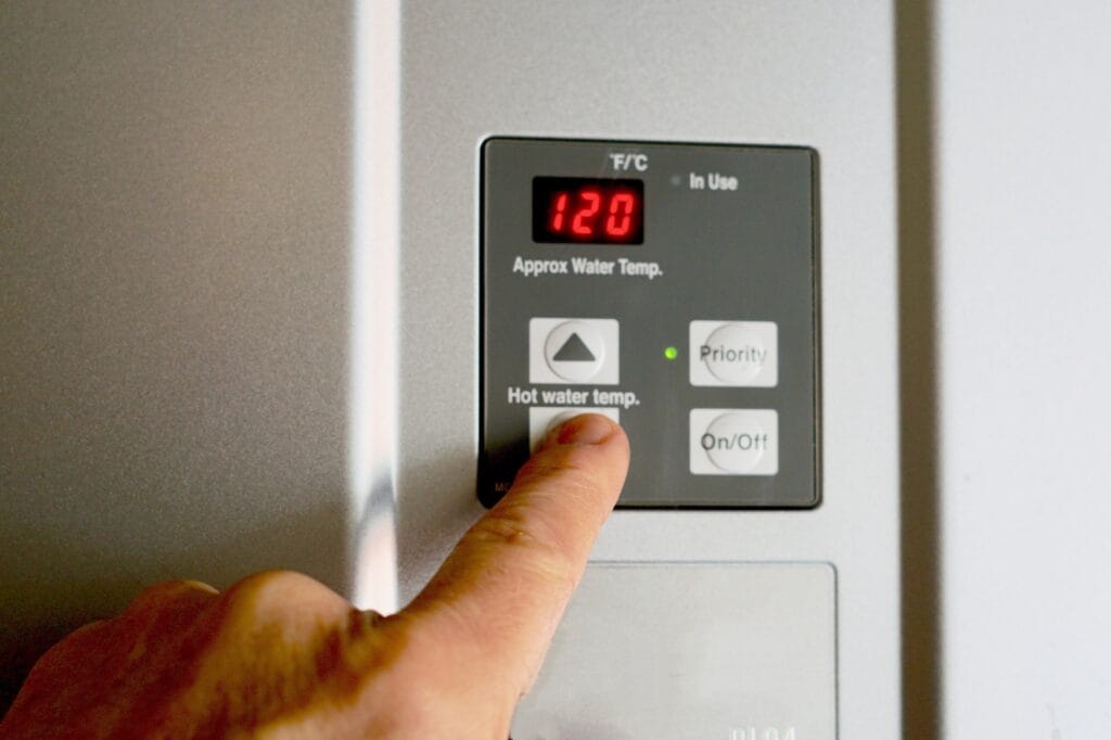 Finger on hot water heater control unit, checking settings while considering when to replace water heater.