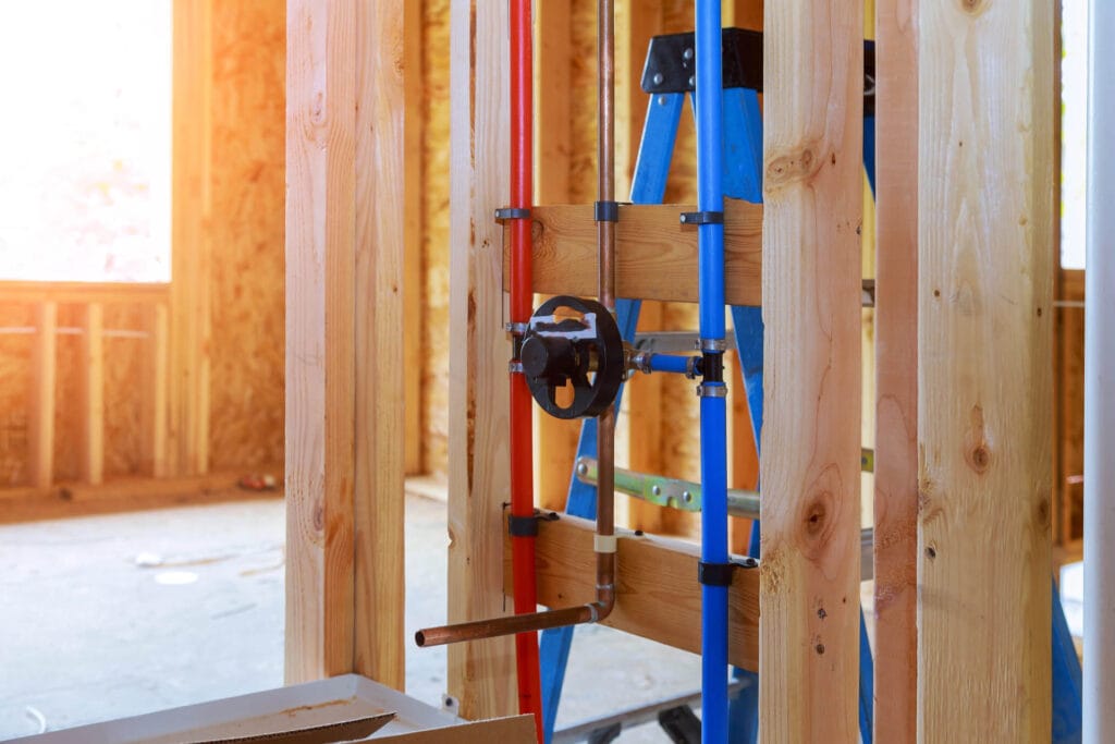 Rough-in plumbing setup with red and blue pipes, wooden framing, and a ladder in a home renovation context, emphasizing plumbing services in Powder Springs, GA.