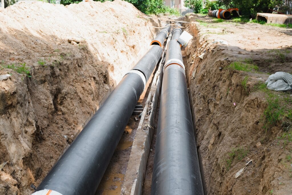 Industrial water pipes installed in a dug trench, showcasing rough-in plumbing for new construction in Dallas, GA, relevant to JW Plumbing Pros' services.