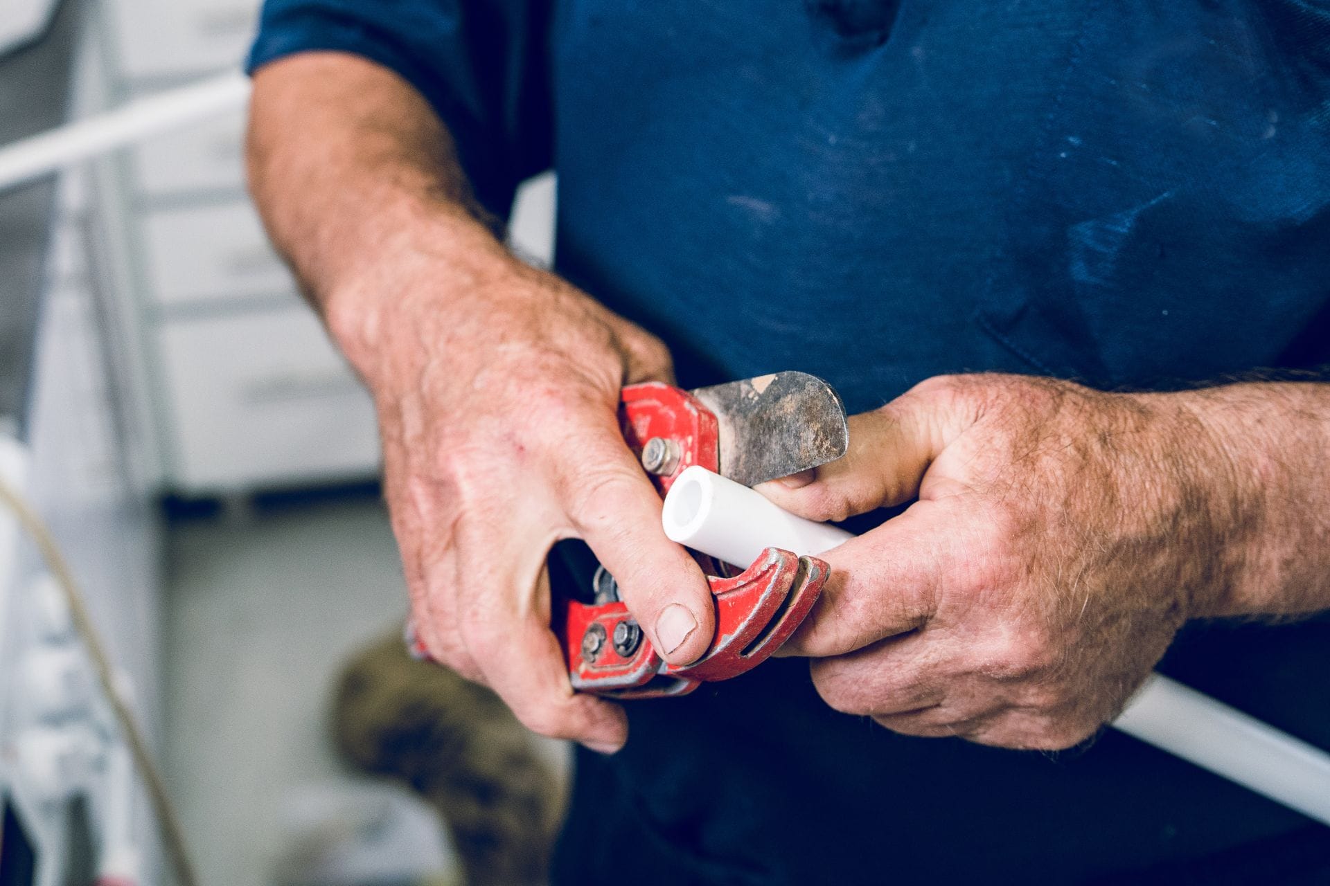 Plumber using red pipe cutter on white PVC pipe, illustrating expert plumbing services by JW Plumbing Pros in Northwest Georgia.