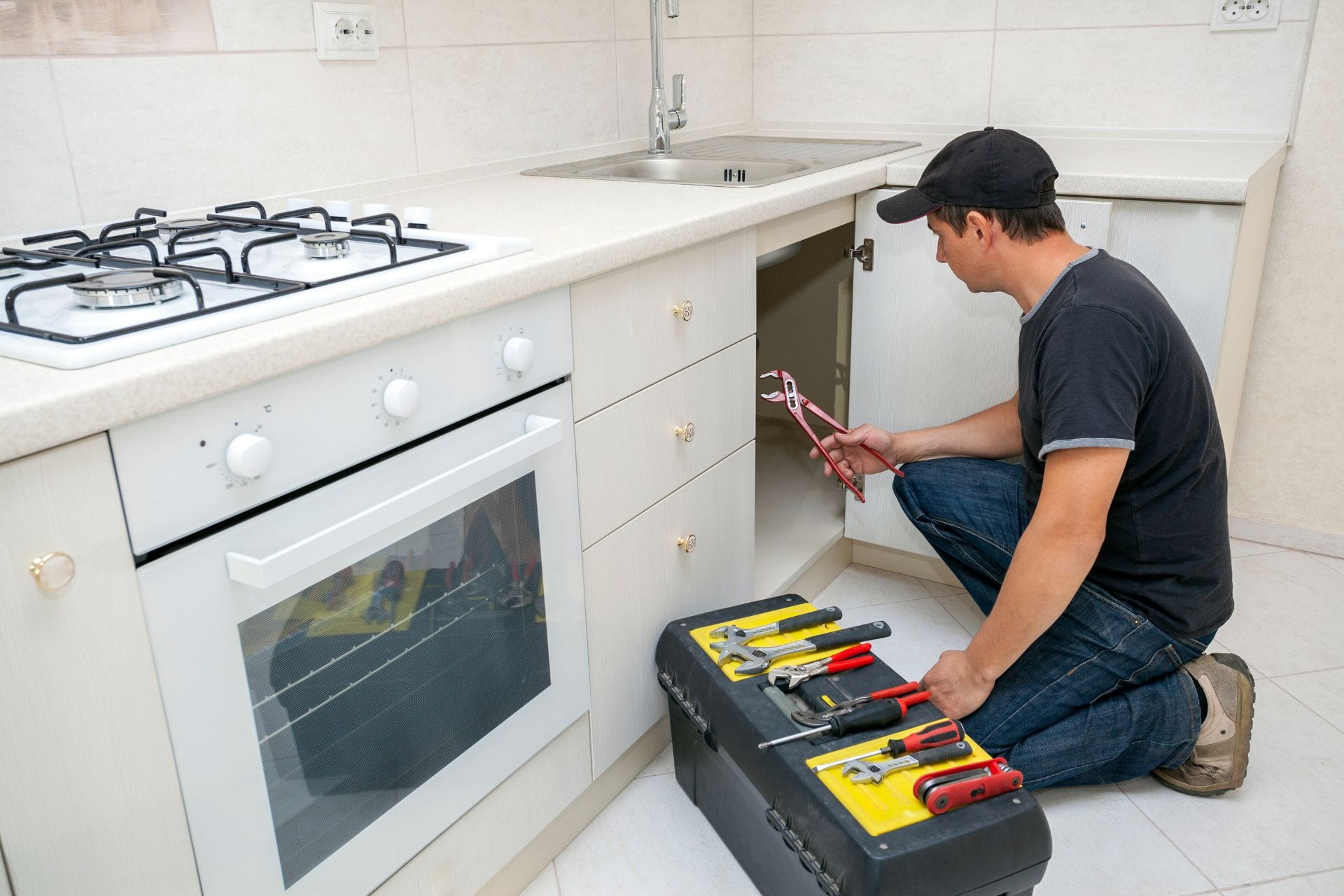Plumber inspecting kitchen cabinet with tools, showcasing residential plumbing services in NorthWest Atlanta.