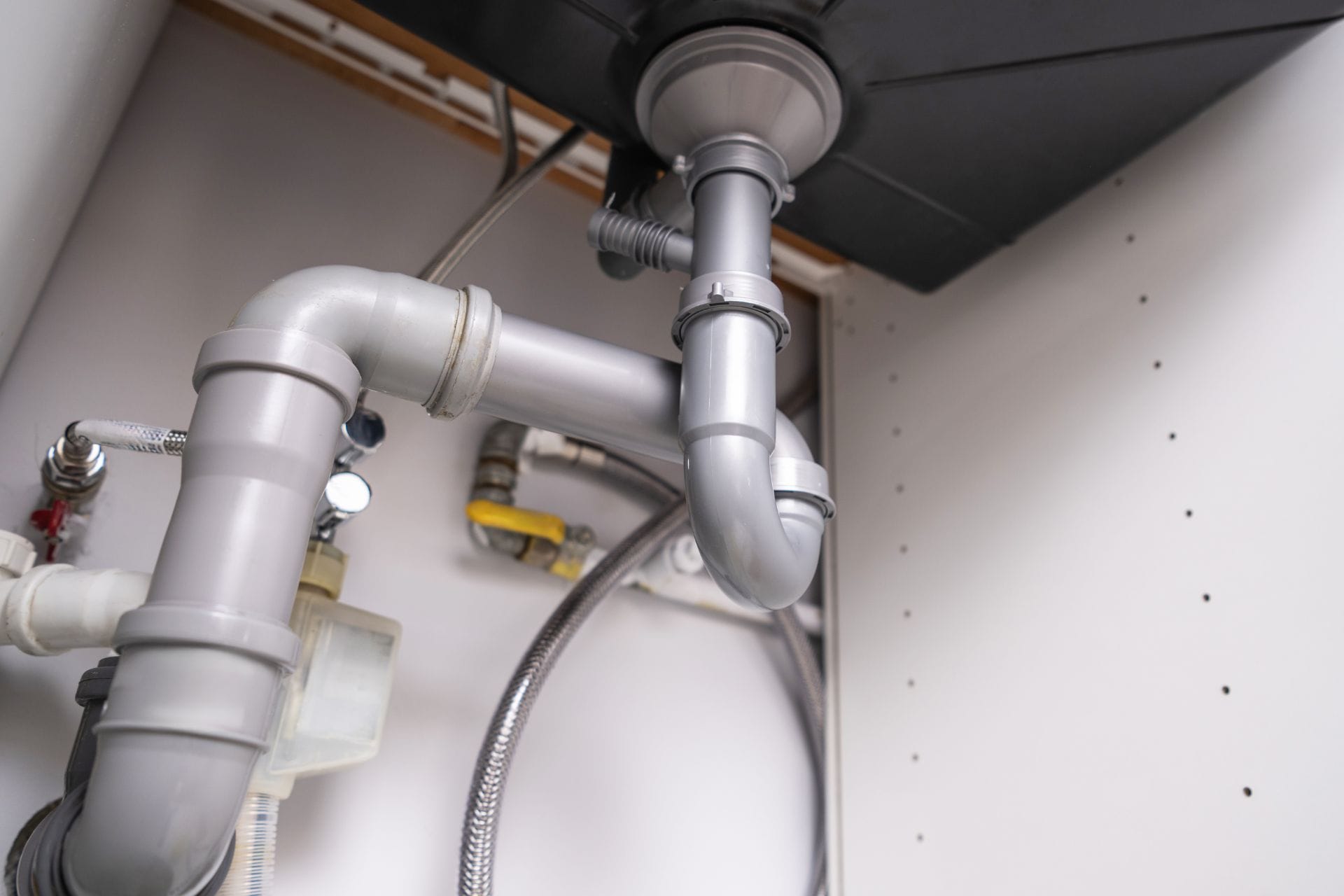 Plumbing pipes and fittings under a sink, showcasing quality plumbing work relevant to JW Plumbing Pros' reliable service.
