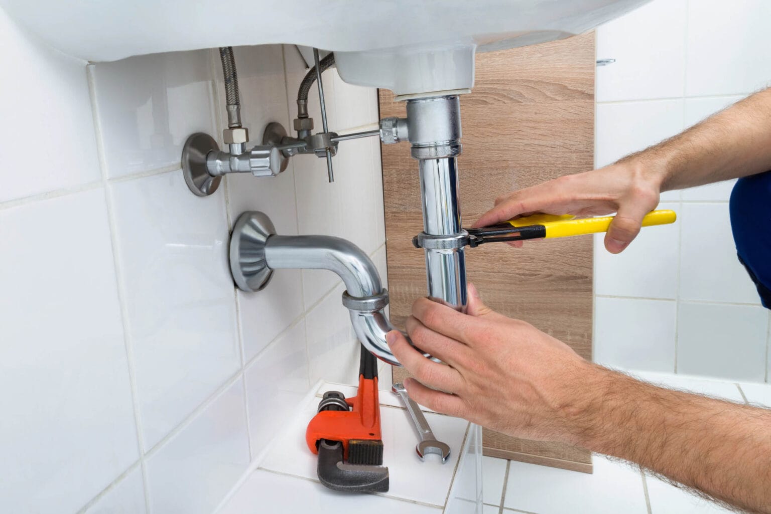 Plumber using tools to repair bathroom plumbing under a sink, demonstrating expertise in toilet repair and installation services.