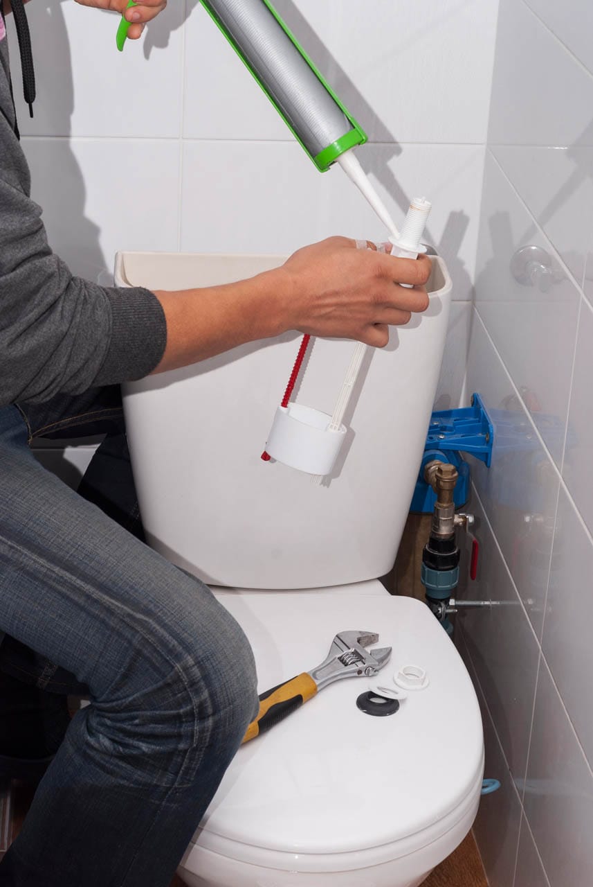 Person repairing a toilet using a wrench and tools, focusing on toilet installation and maintenance in a residential bathroom setting.