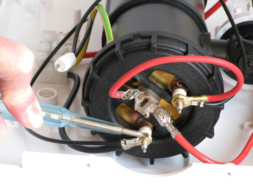 Hand holding a screwdriver while working on electrical connections inside a water heater, showcasing repair and maintenance processes relevant to plumbing services.