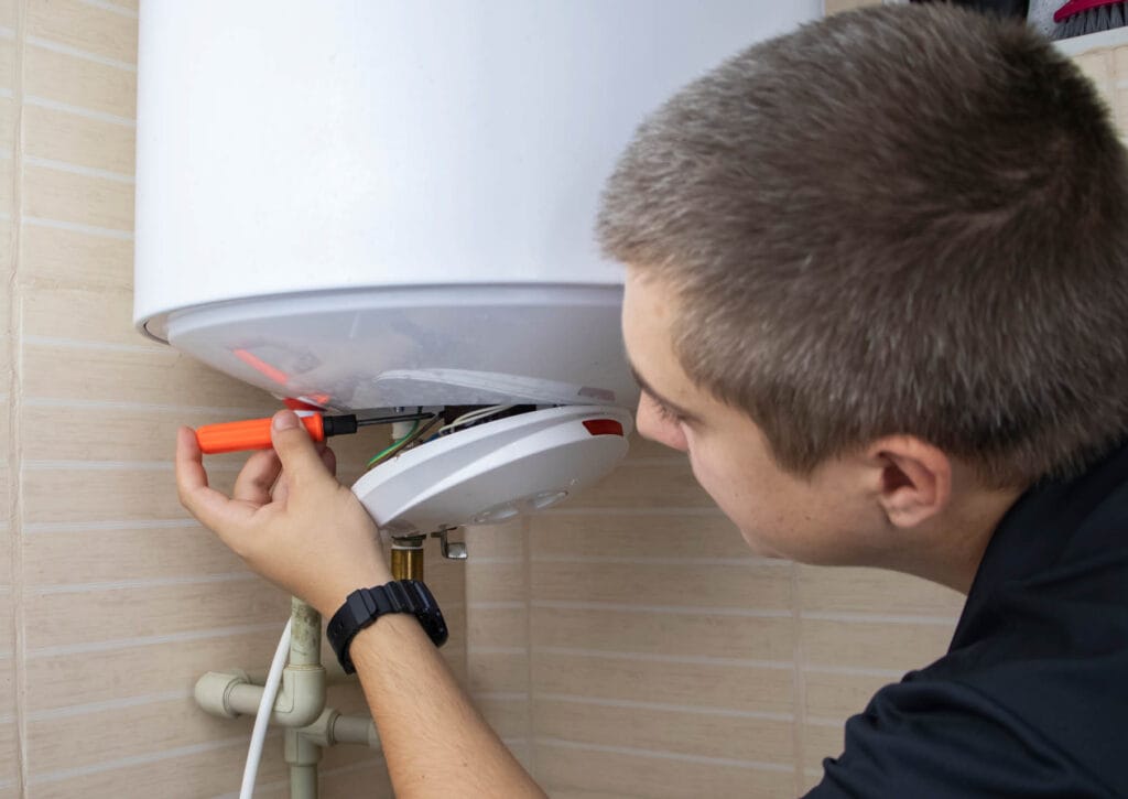 Technician performing maintenance on a water heater, using a screwdriver to inspect components, illustrating expert water heater repair services in Austell, GA.