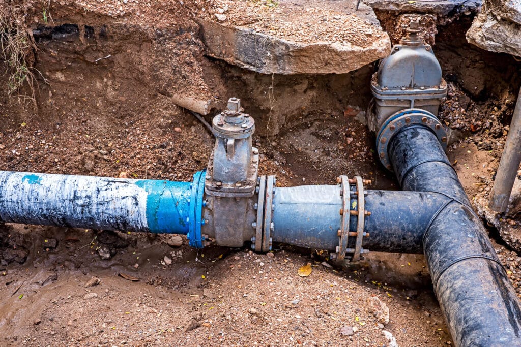 Damaged water lines with blue and black pipes exposed in a trench, illustrating plumbing repair services offered by JW Plumbing Pros in Powder Springs, GA.