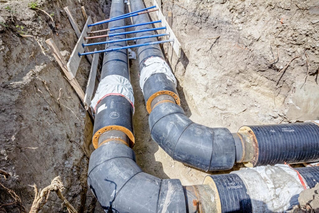 Water line installation with large black pipes in a trench, showcasing plumbing work related to leak detection and repairs.
