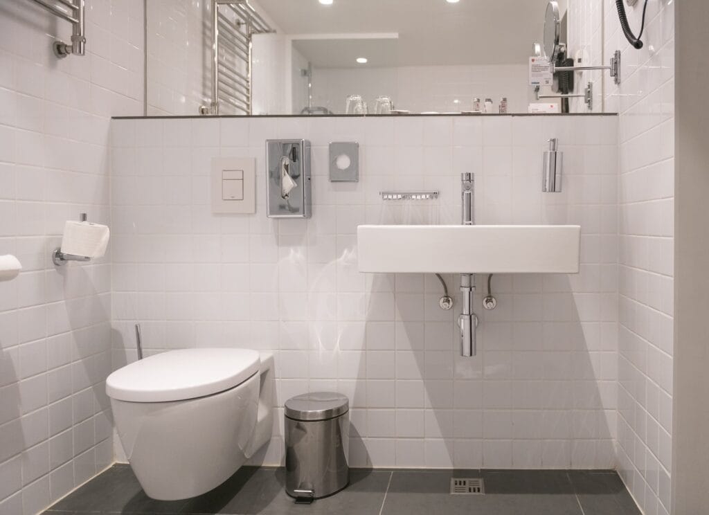 Modern white bathroom featuring a wall-mounted sink, sleek toilet, and minimalist design elements, emphasizing plumbing efficiency and aesthetic appeal.