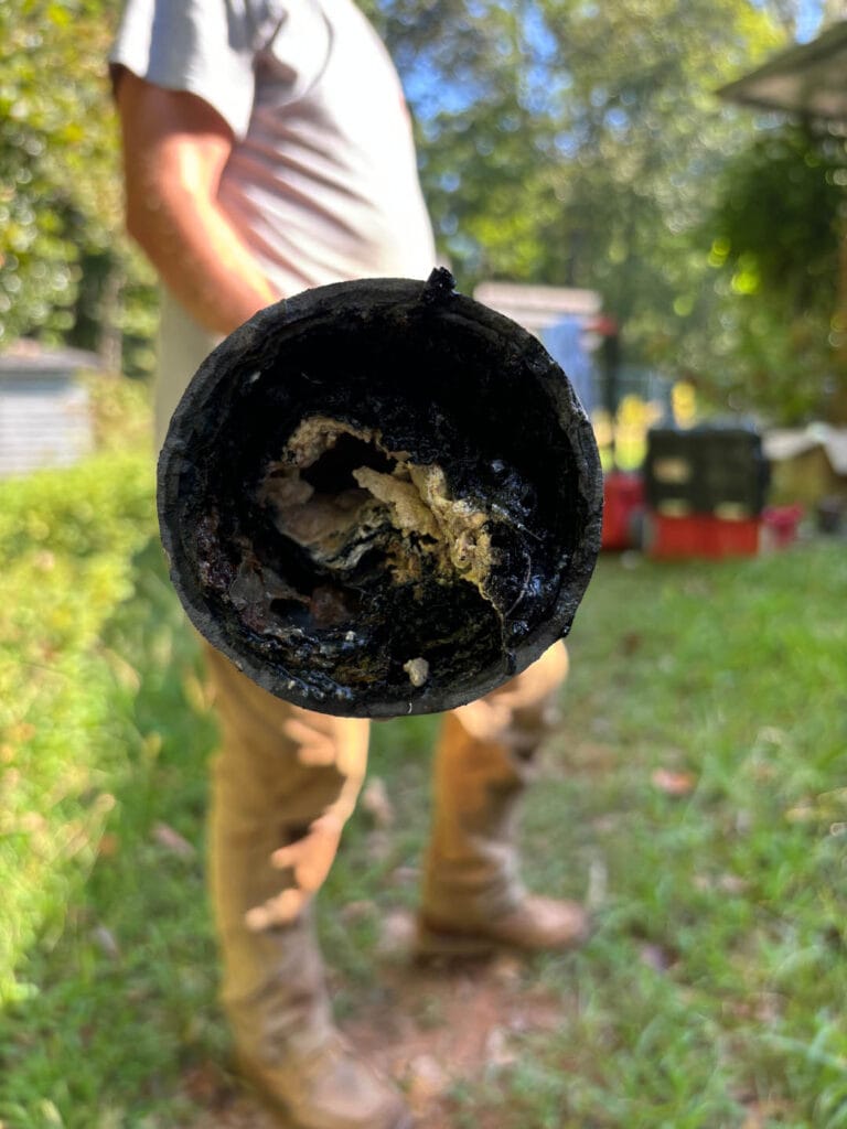 Person holding a corroded pipe with buildup inside, standing on grass.