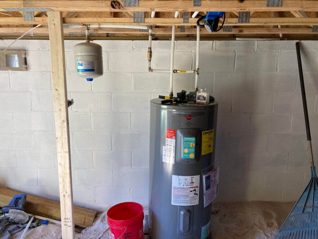 Water heater installation in a utility space, featuring a gray water heater with visible labels and a nearby pressure tank, surrounded by construction materials and tools, relevant to water heater repair services in Austell, GA.