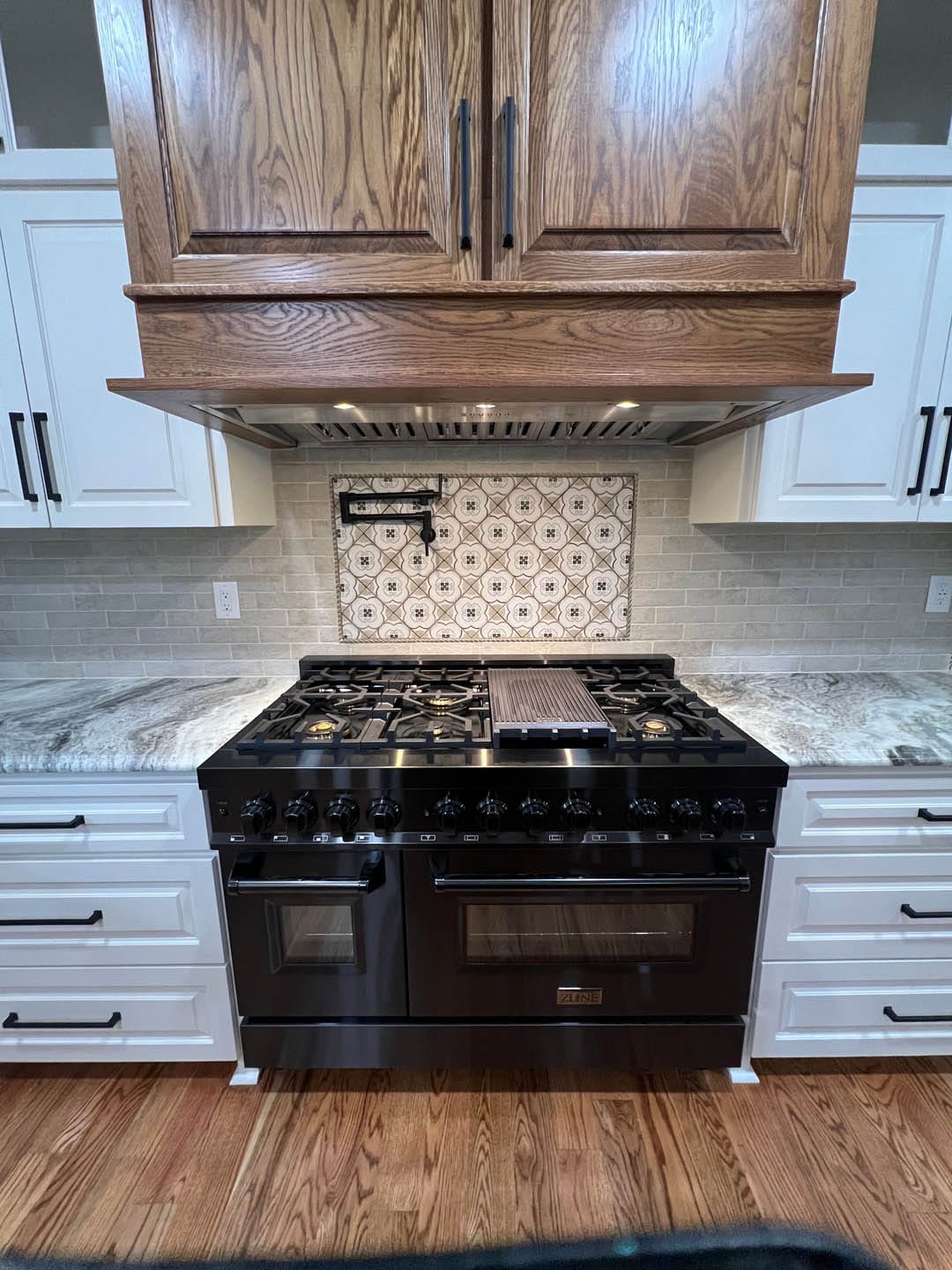 Modern kitchen featuring a black gas range with dual ovens, stylish wooden cabinetry, and elegant backsplash tiles, emphasizing quality craftsmanship and attention to detail in residential plumbing renovations by JW Plumbing Pros.