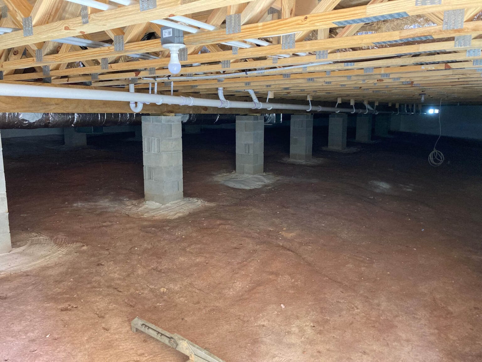 New home construction crawl space with visible plumbing pipes, wooden beams, and concrete supports, illustrating plumbing infrastructure importance for reliable home comfort and maintenance.