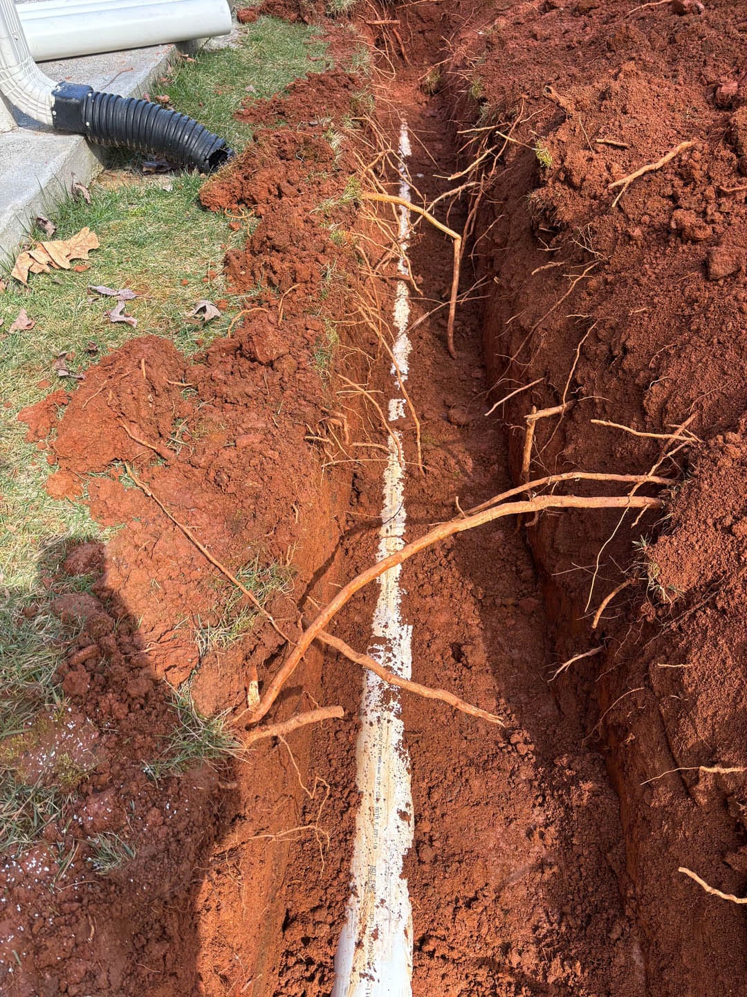 Trenched area revealing a damaged water line surrounded by red clay soil and tree roots, illustrating the need for expert water line repair services in Atlanta, GA.