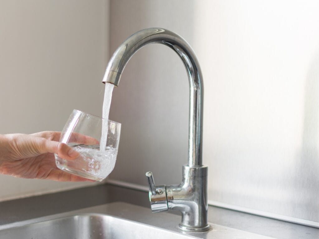 Hand pouring water from a kitchen faucet into a glass, illustrating water flow and pressure issues relevant to plumbing concerns.