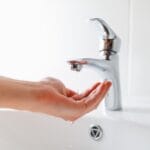 Hand reaching for a bathroom faucet, illustrating low water pressure issues relevant to plumbing problems and maintenance tips.
