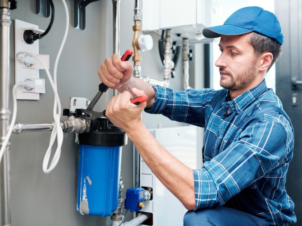 Plumber using tools to inspect and repair water filtration system, demonstrating advanced leak detection techniques in residential plumbing.
