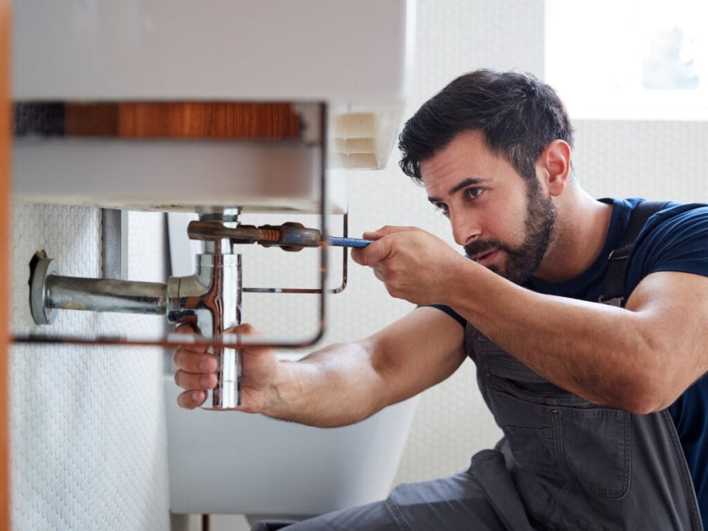 Plumber repairing a sink drain under a bathroom cabinet, demonstrating professional plumbing services for recurring drain clogs in Northwest Georgia.