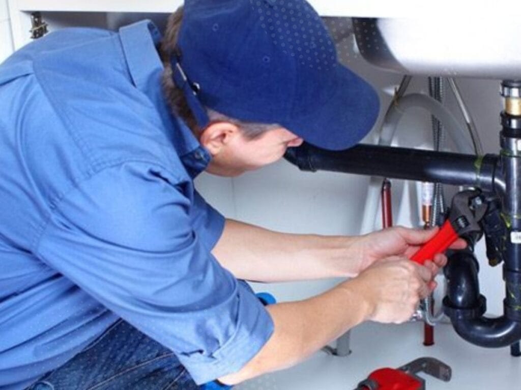 Plumber using adjustable wrench to fix drain pipes under a sink, illustrating maintenance to prevent recurring clogs in plumbing systems.
