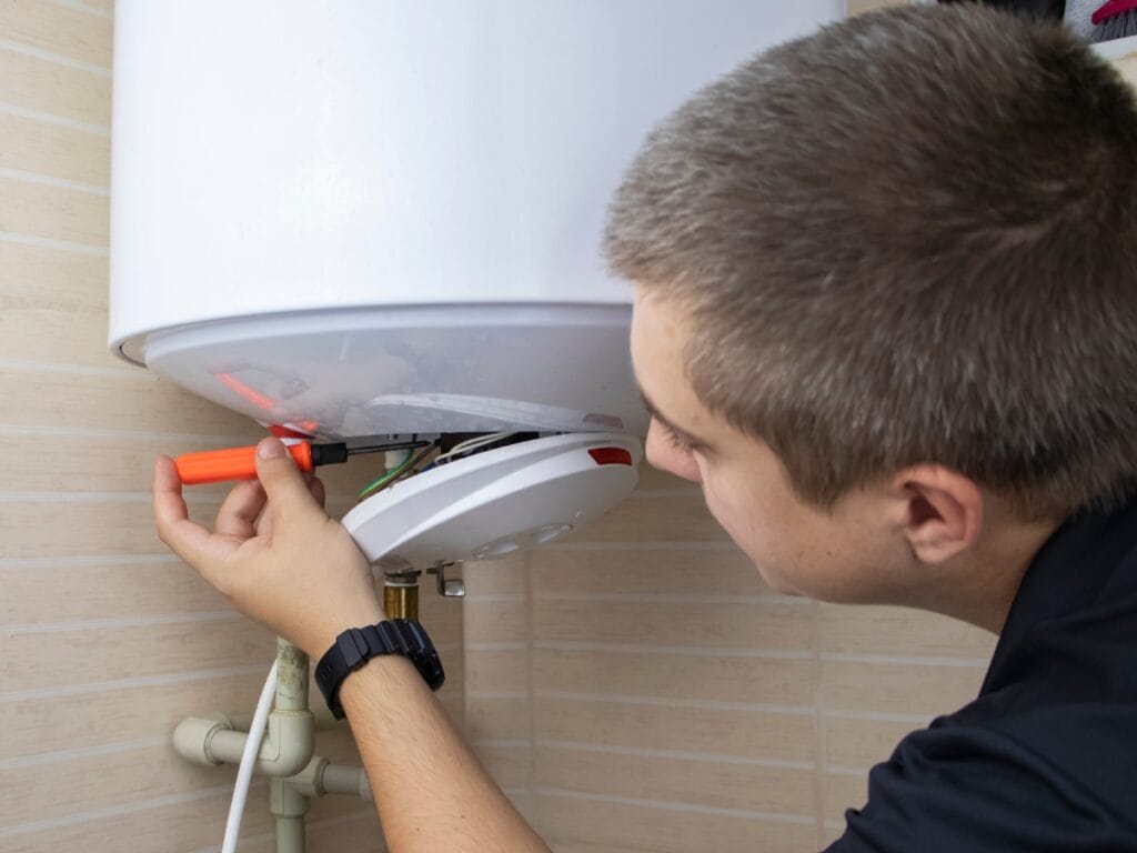 Technician performing maintenance on a water heater, inspecting the temperature-pressure relief valve with a screwdriver, emphasizing the importance of regular checks for safety and efficiency.