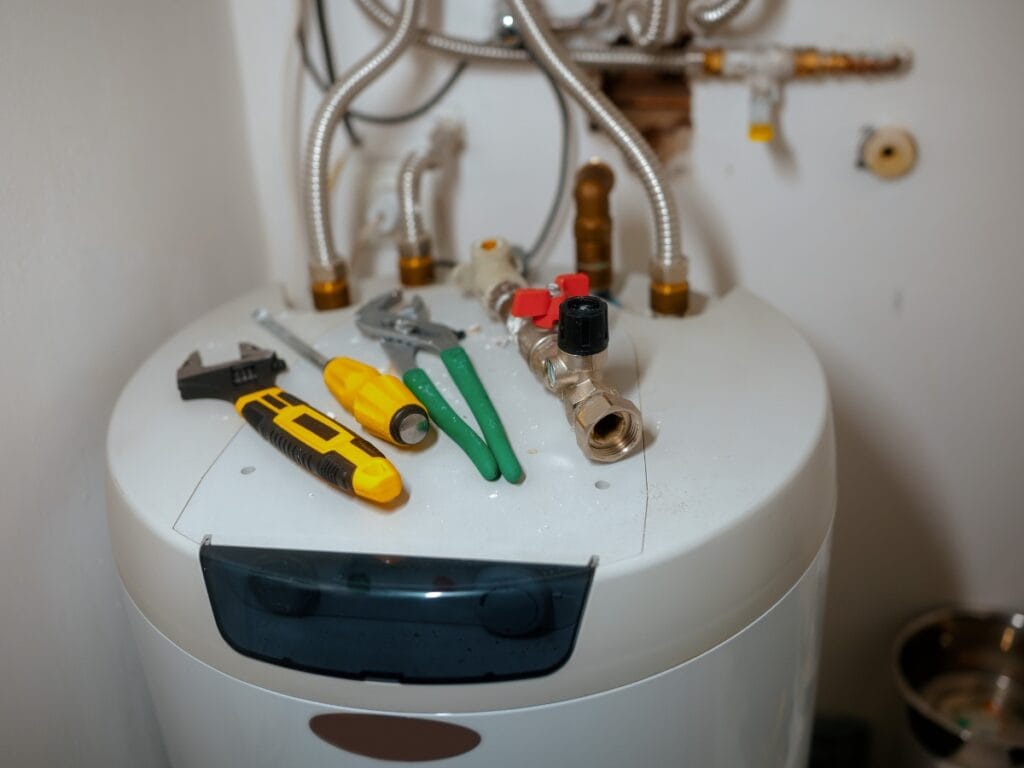 Tankless water heater with tools including wrenches and screwdrivers, illustrating maintenance and repair aspects relevant to energy-efficient plumbing solutions.