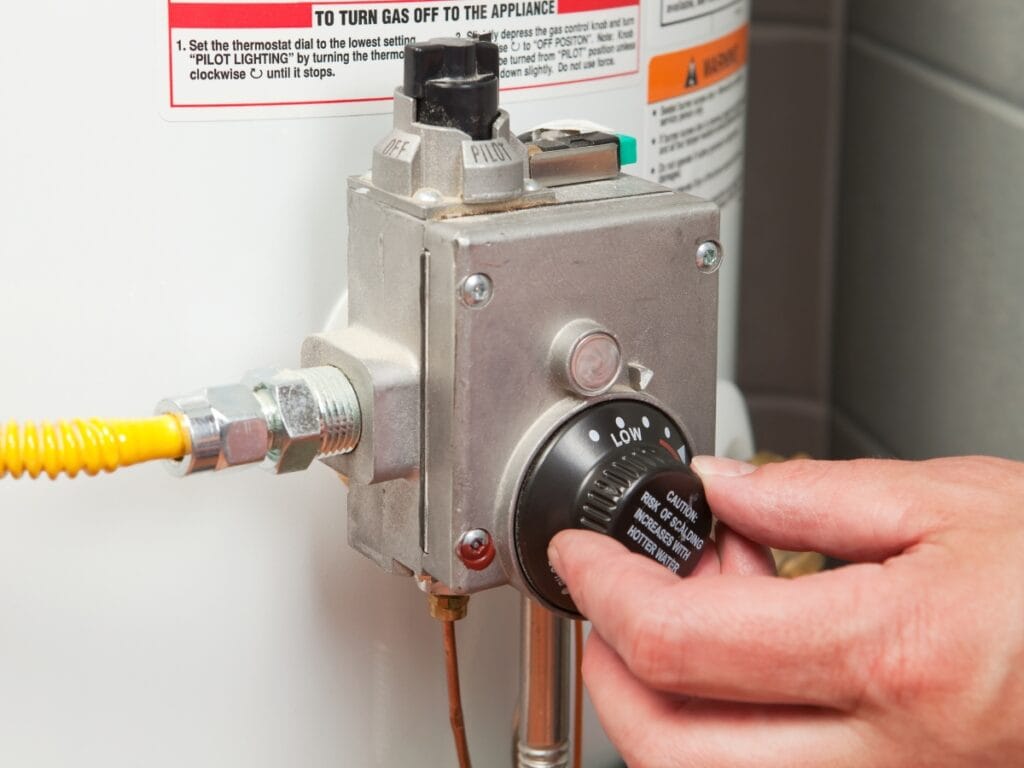Hand adjusting the gas control knob on a tankless water heater, highlighting energy-efficient hot water solutions for modern homes.