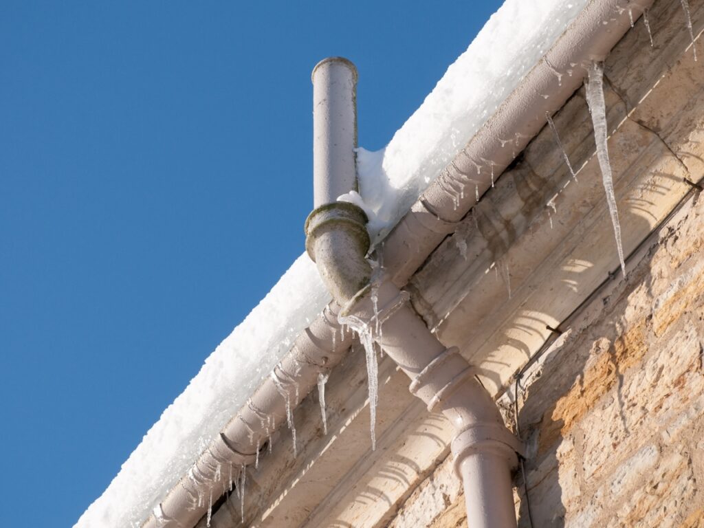 Icicles forming on frozen pipes at the edge of a roof, illustrating potential plumbing issues in winter weather.