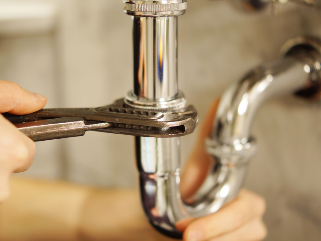 A person uses a wrench to tighten a metal pipe under a sink, ensuring proper backflow prevention.