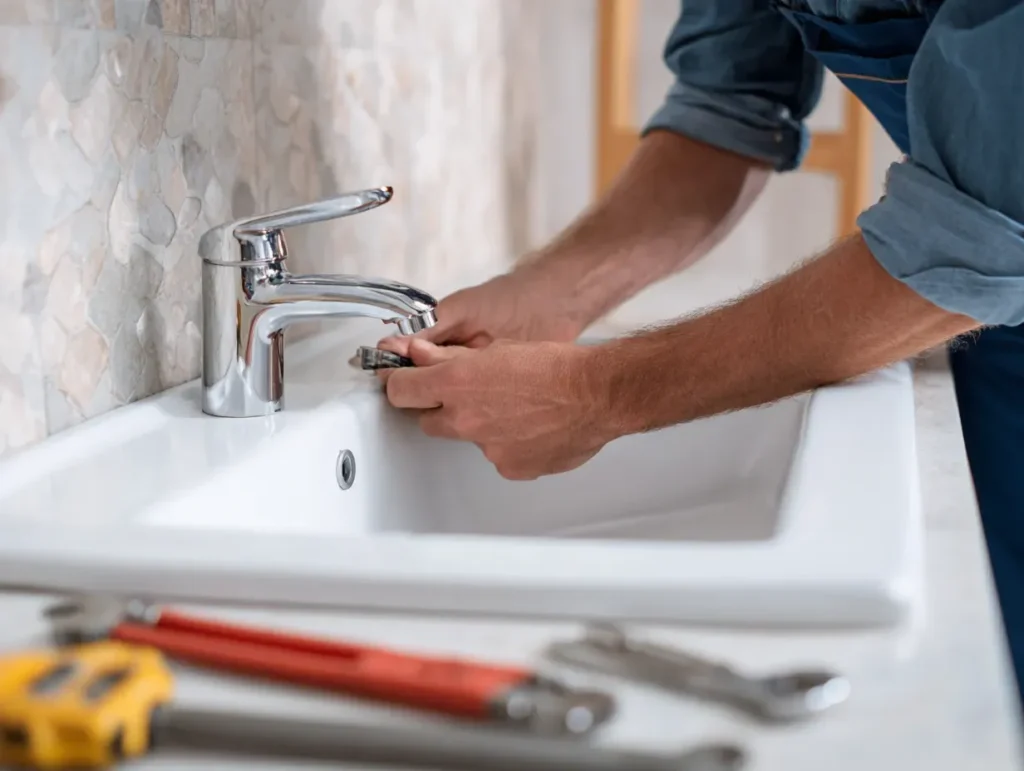 Person repairing a chrome faucet at a bathroom sink.