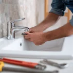 Person repairing a chrome faucet at a bathroom sink.